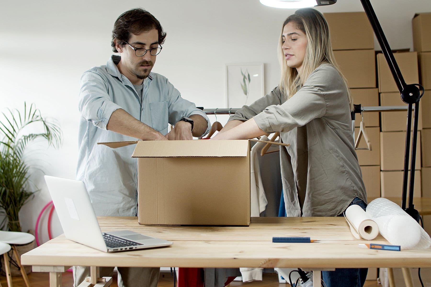 Two people packing a cardboard box at a table, with a laptop open beside them