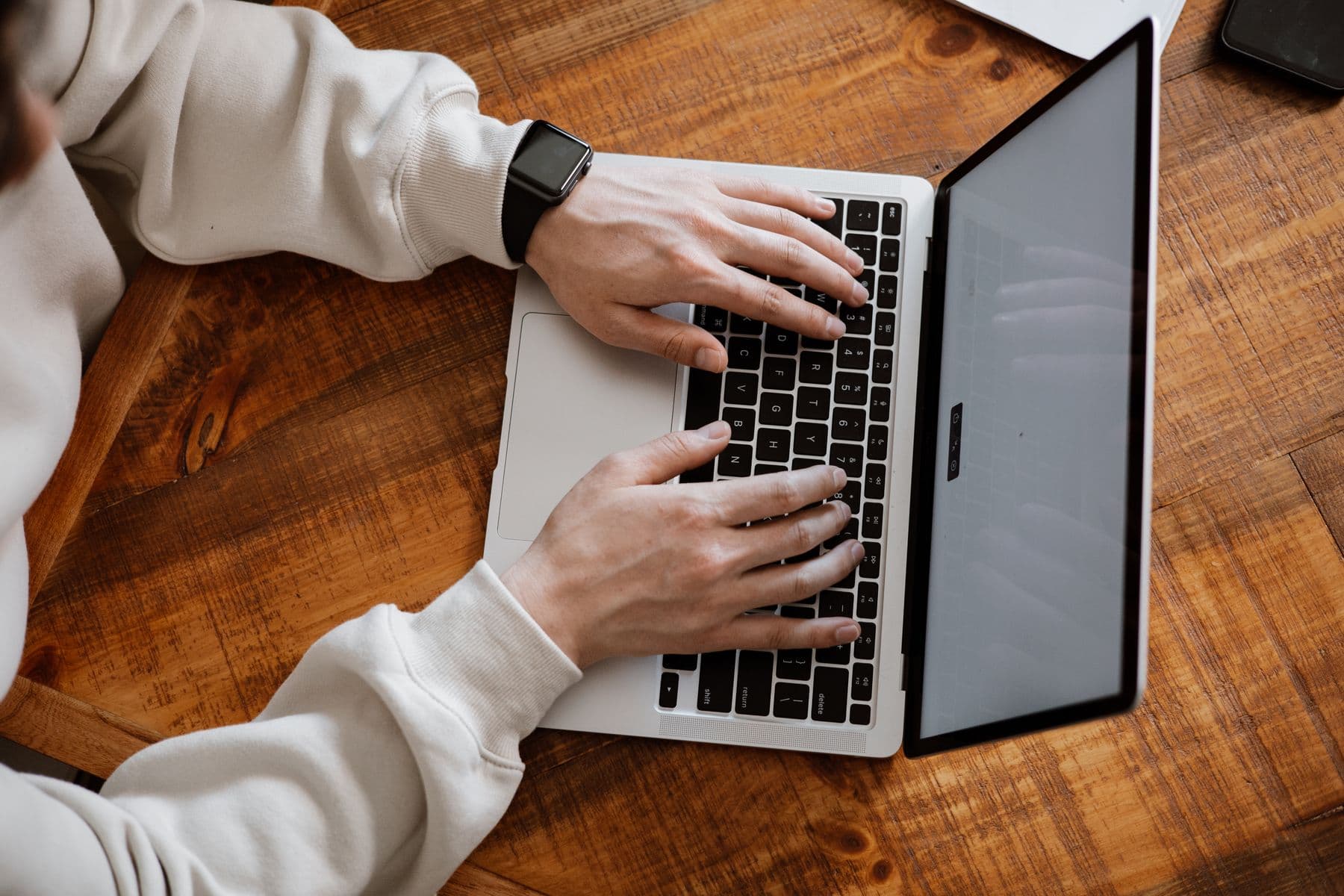 Hands typing on a laptop on a wooden desk