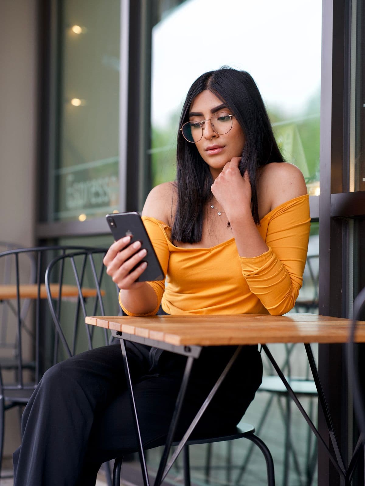 A woman at an outdoor café table looking at a phone