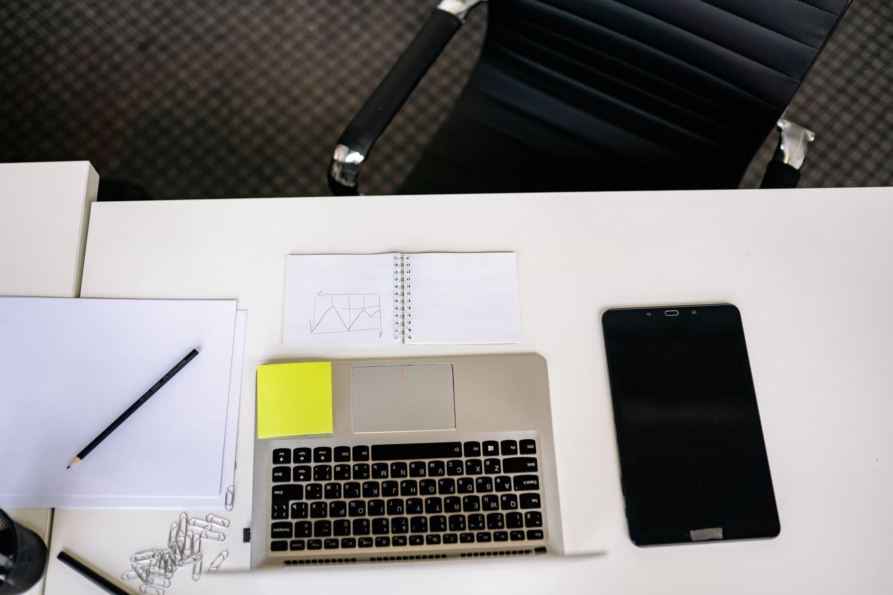 A laptop and a tablet on a white desk, with a notebook and a pencil